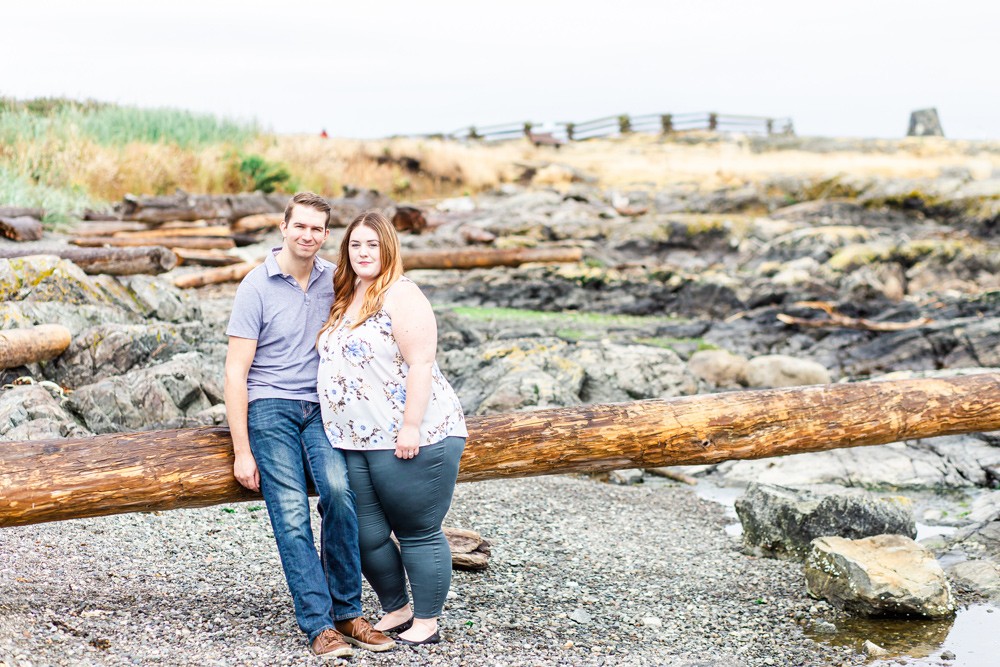 Couple leaning on a log on a rocky vancouver island beach in oak bay